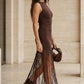 Woman wearing a brown sleeveless dress with fringe details in an architectural setting.